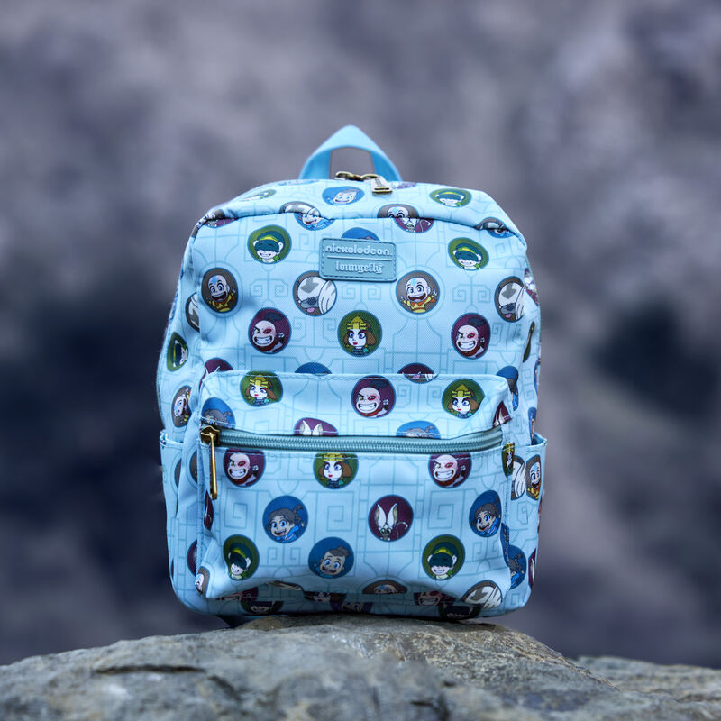 Blue Loungefly Avatar: The Last Airbender All-Over Print Nylon Square Mini Backpack featuring an all-over print of circles with different characters from Avatar: The Last Airbender on it, connected by a light blue elemental motif. The bag sits on a rock outside. 